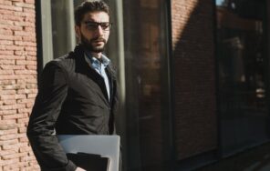 メガネをかけてノートパソコンを持ち街を歩く人のイメージ