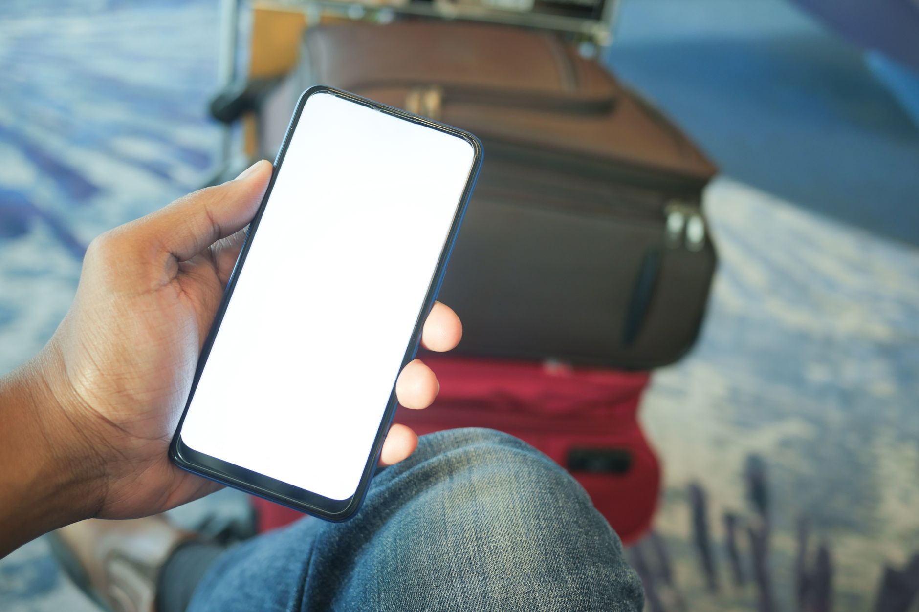 空港でスーツケースを横に置きスマートフォンを操作している旅行者のイメージ