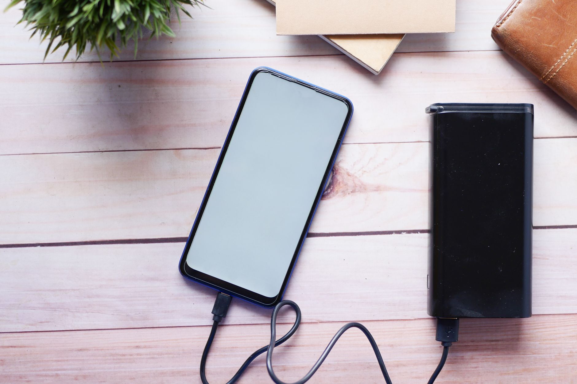 木製デスクの上でモバイルバッテリーからスマートフォンを充電するイメージ