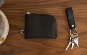 木製のテーブルに置かれた黒い革の財布と鍵のイメージ