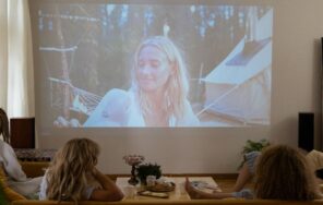 照明を落としたリビングのソファに座り、壁に投影された映像を見ている人たちのイメージ