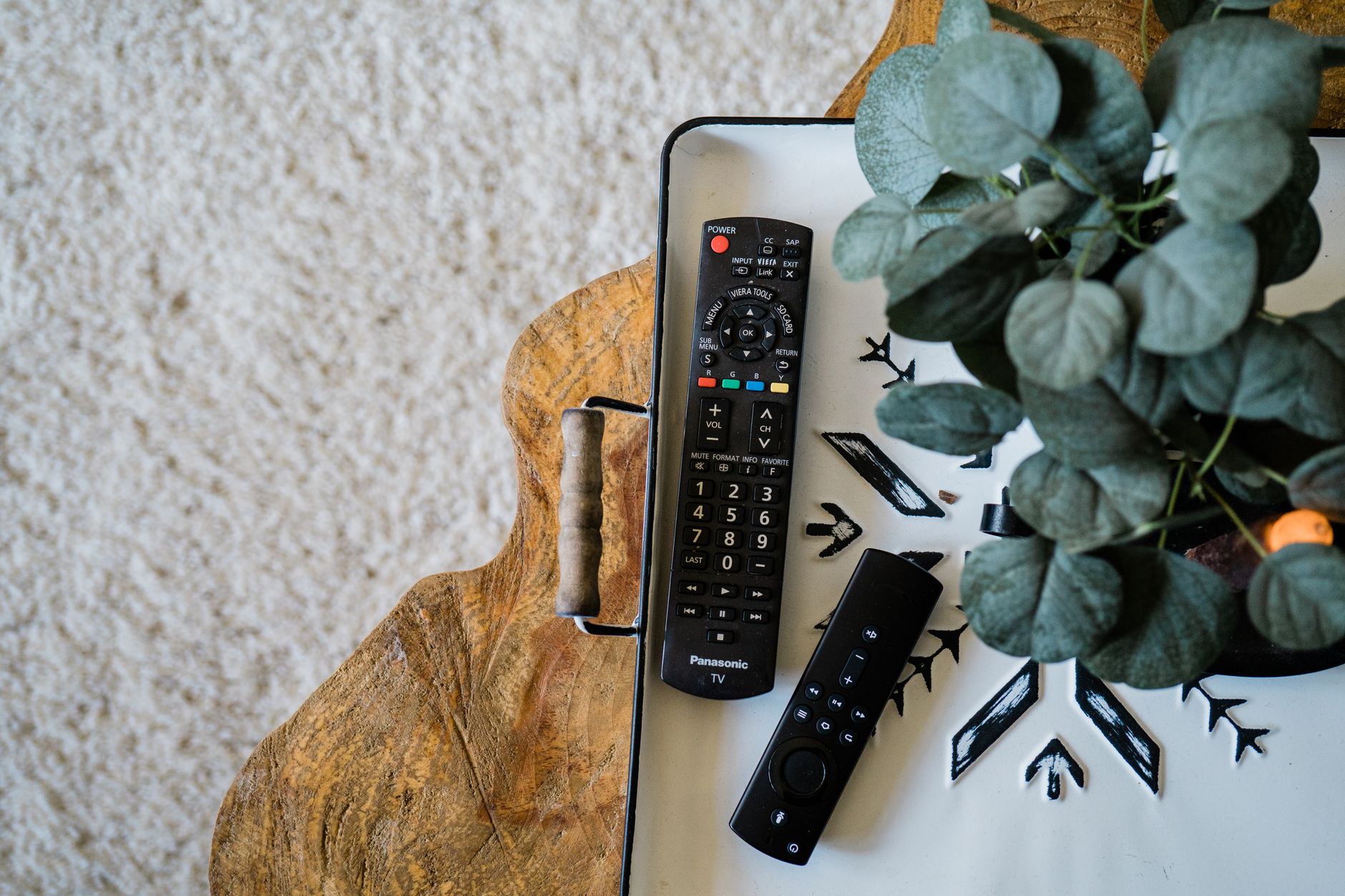 木製のテーブルに並べて置かれた2本のテレビリモコンと観葉植物のイメージ