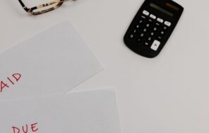 支払い済みと未払いの書類と電卓を並べた机のイメージ