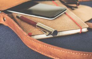 革のカバンに入ったノートとペンとスマートフォンのイメージ