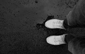 Top view of a person wearing sneakers standing on wet pavement, creating an artistic scene.