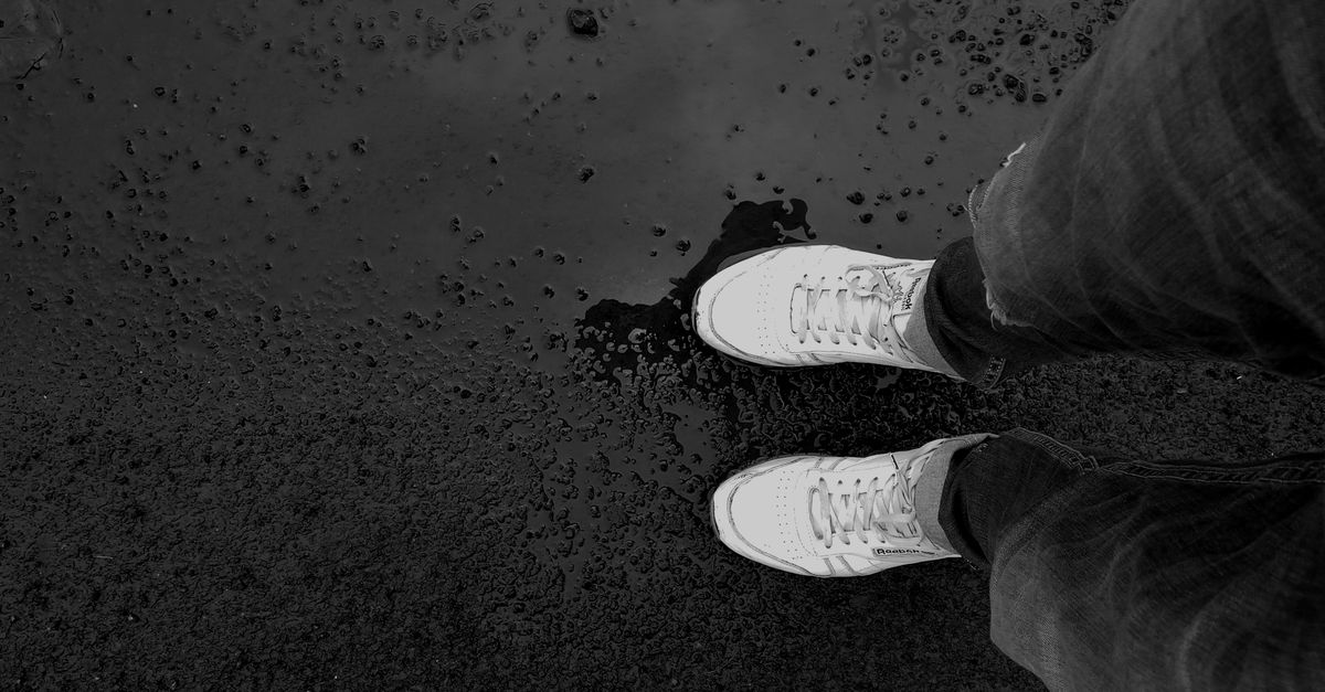 Top view of a person wearing sneakers standing on wet pavement, creating an artistic scene.