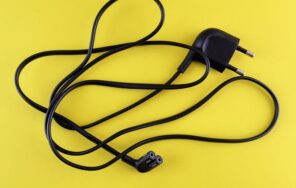 Close-up of a tangled black power cord placed on a vibrant yellow background.