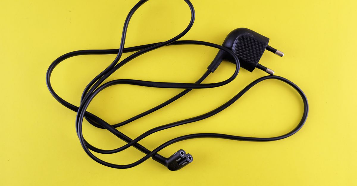 Close-up of a tangled black power cord placed on a vibrant yellow background.